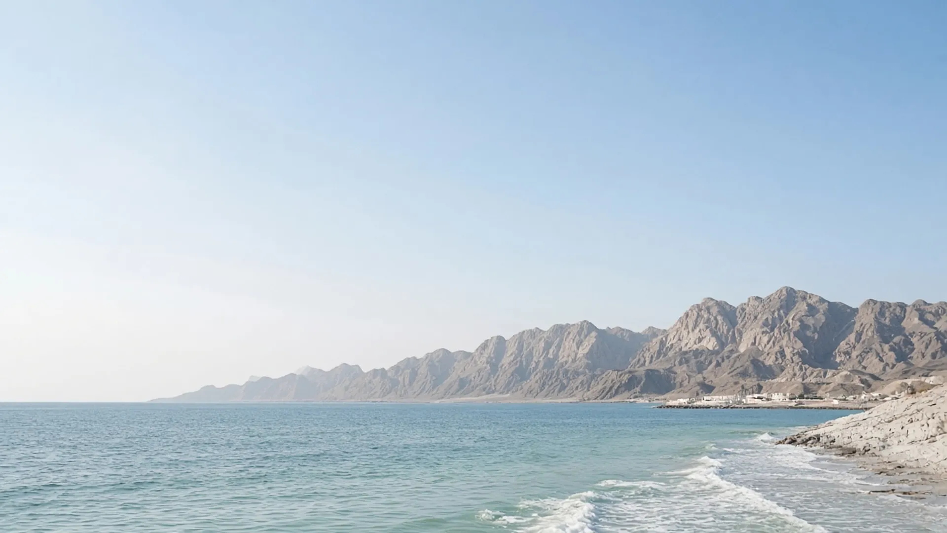 Calm Omani sea meeting rugged mountains at first light
